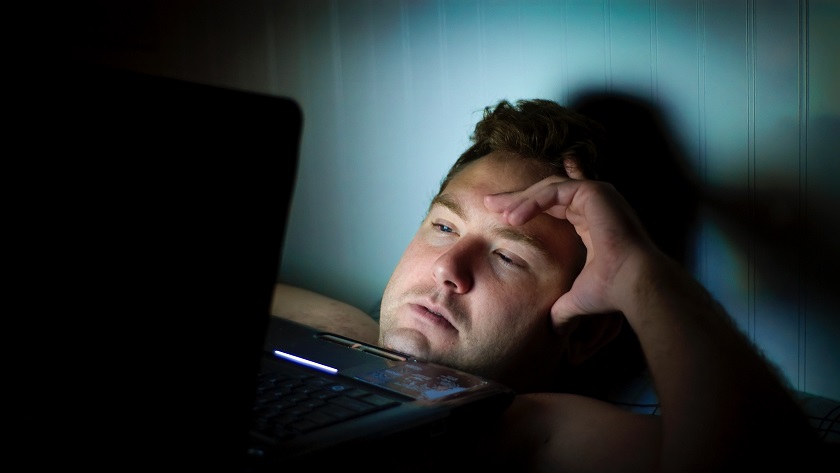 Image of an overtired man in bed using a laptop