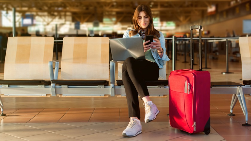 Woman at an airport on a mobile phone with a red suitcase
