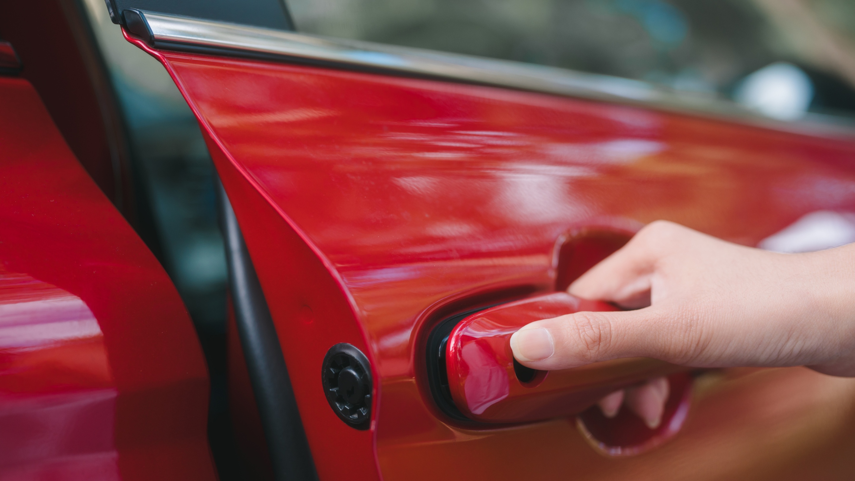 Close-up of a hand pulling the handle to open the door of a red car.
