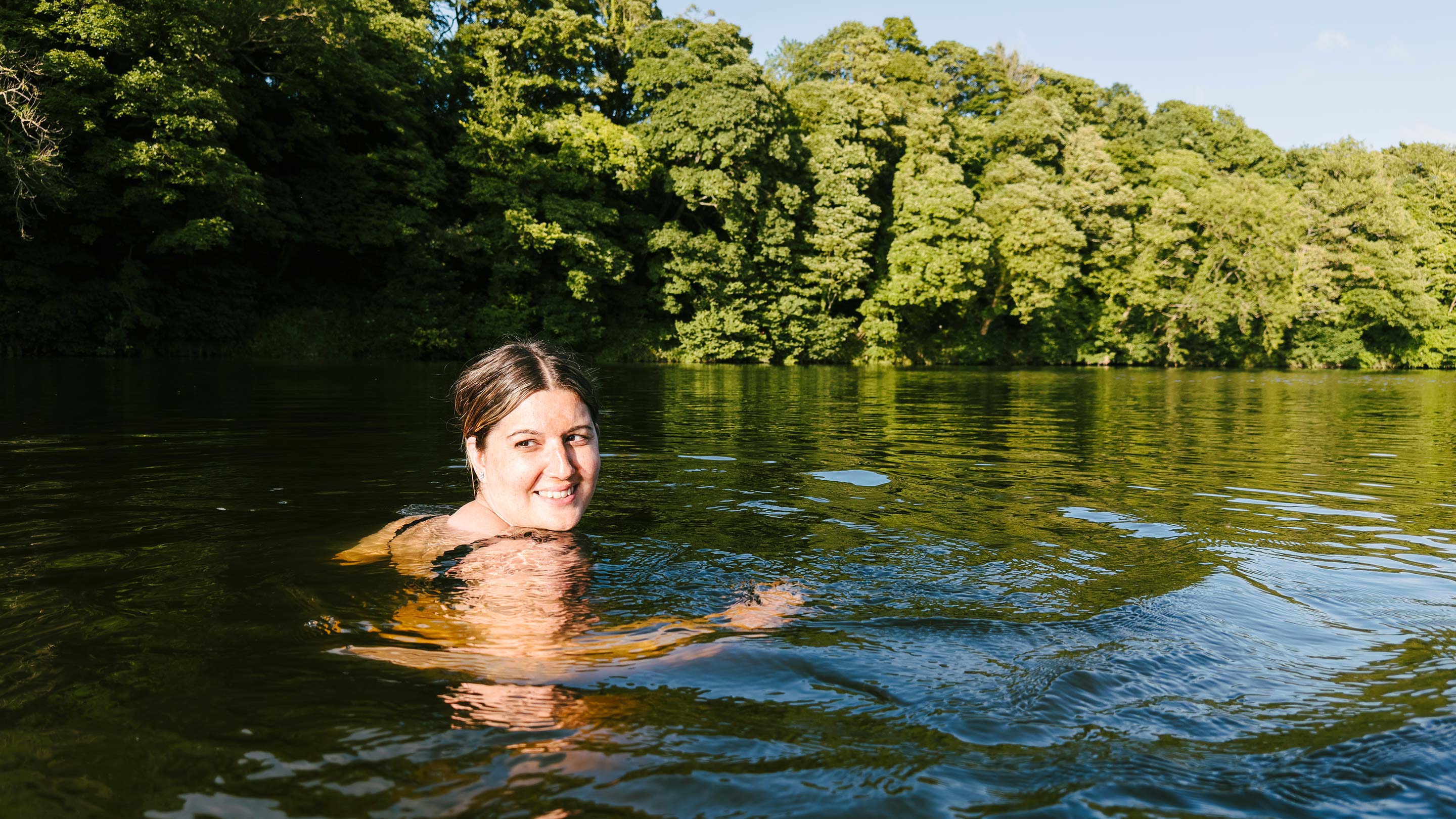 Happy wild swimmer in the river at sunset