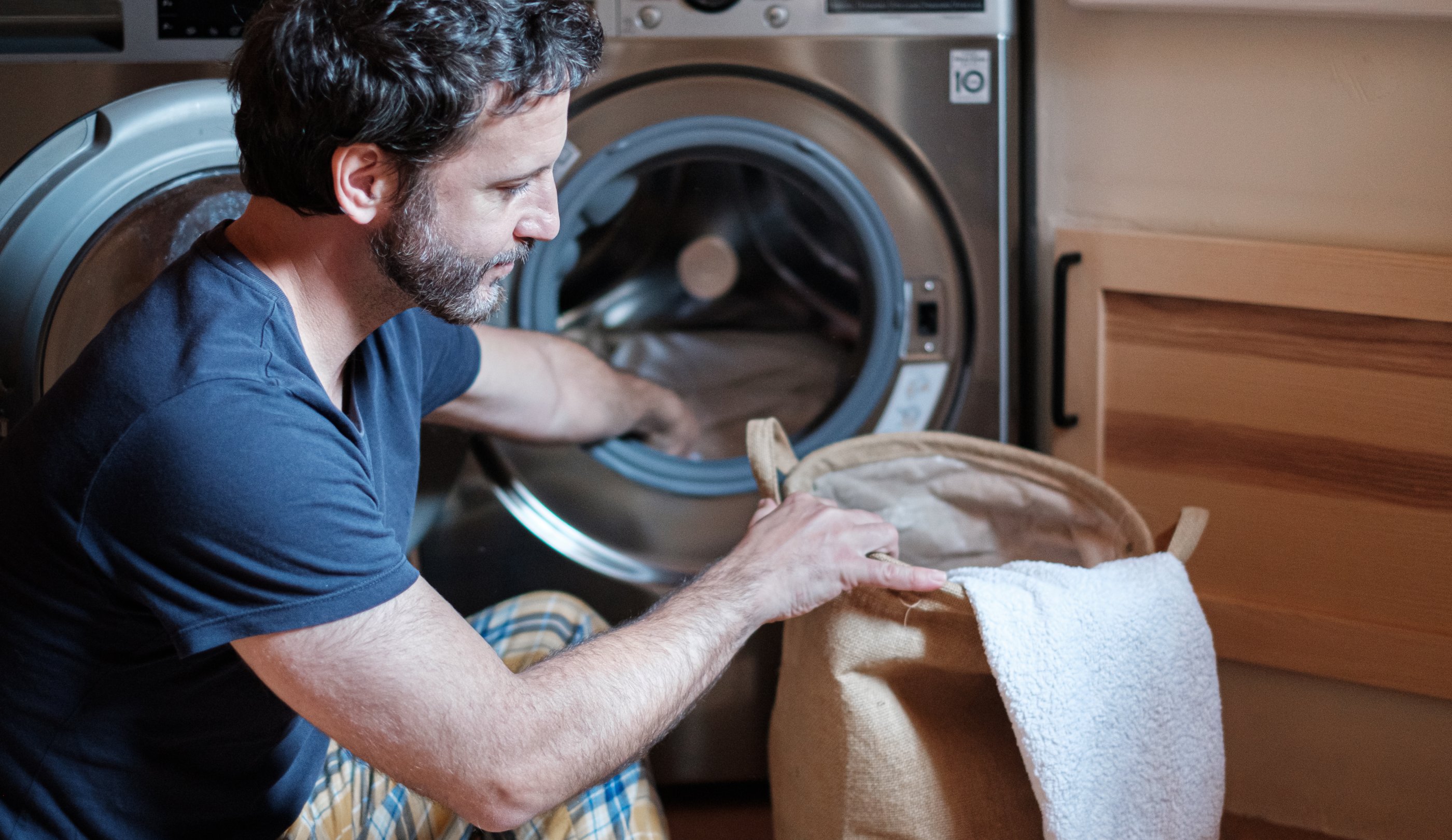 Housekeeper man doing the laundry with open washing machine