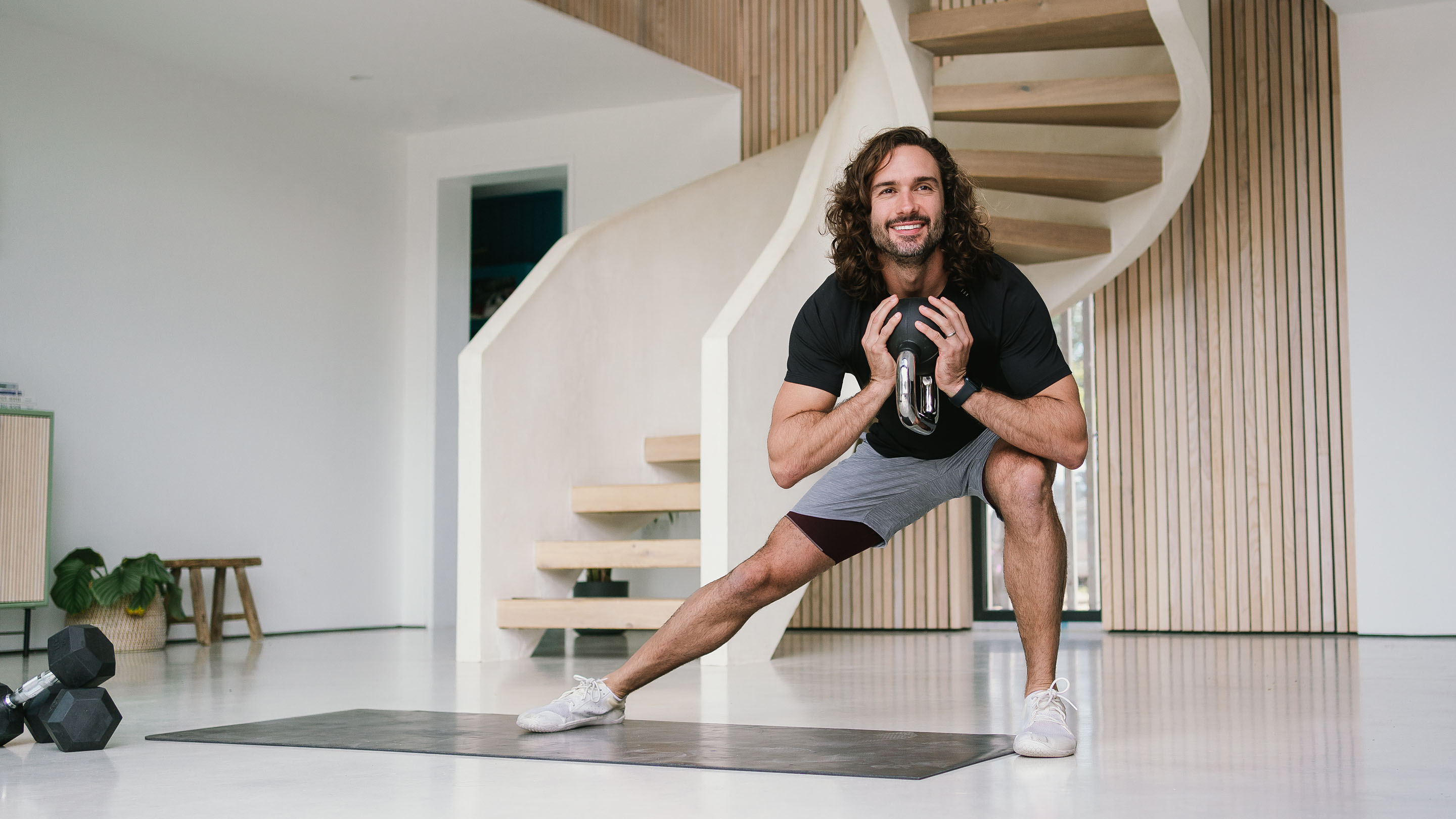 Joe Wicks exercising with a kettlebell in a modern looking room