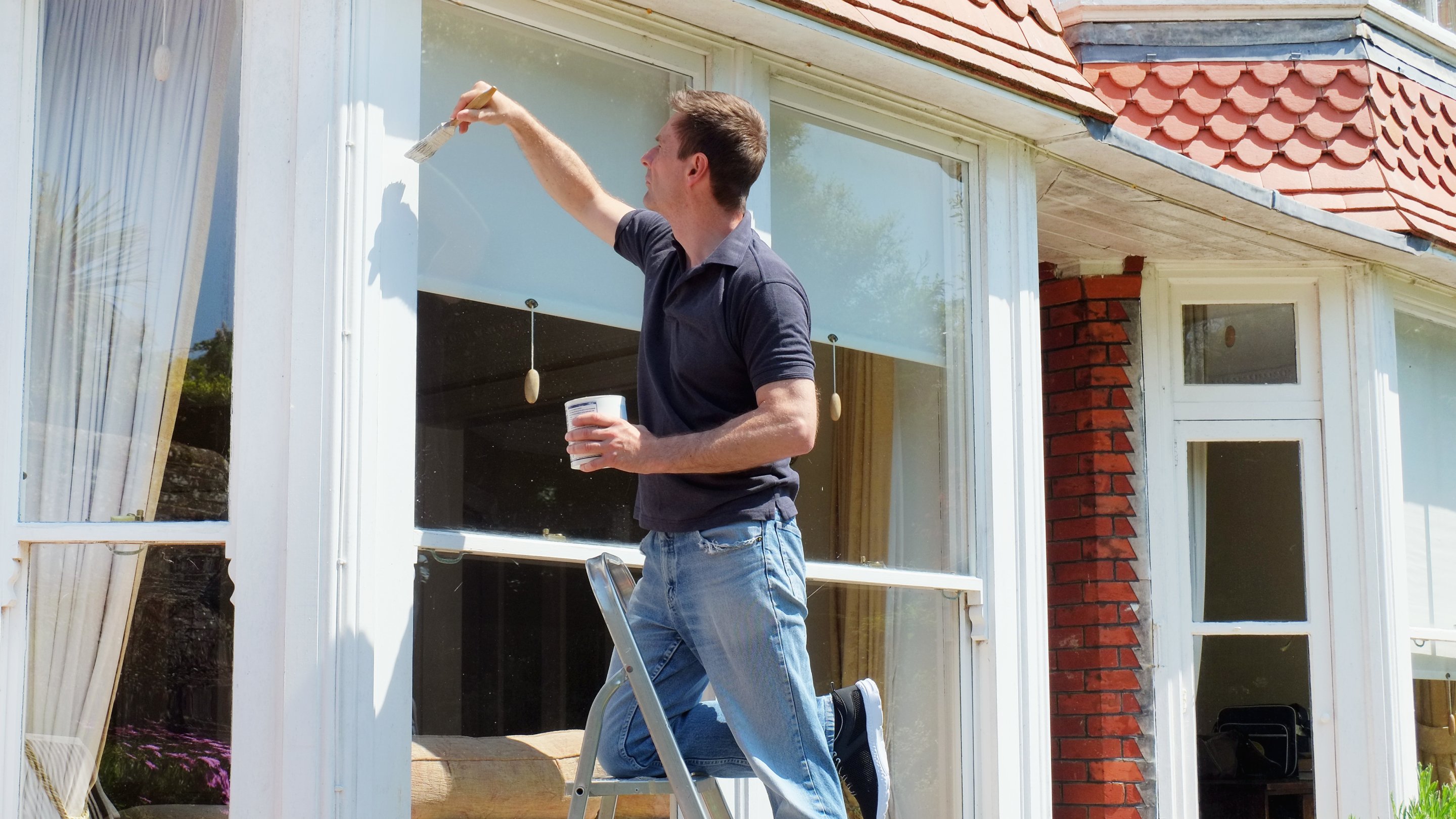 Man on a ladder painting a window frame