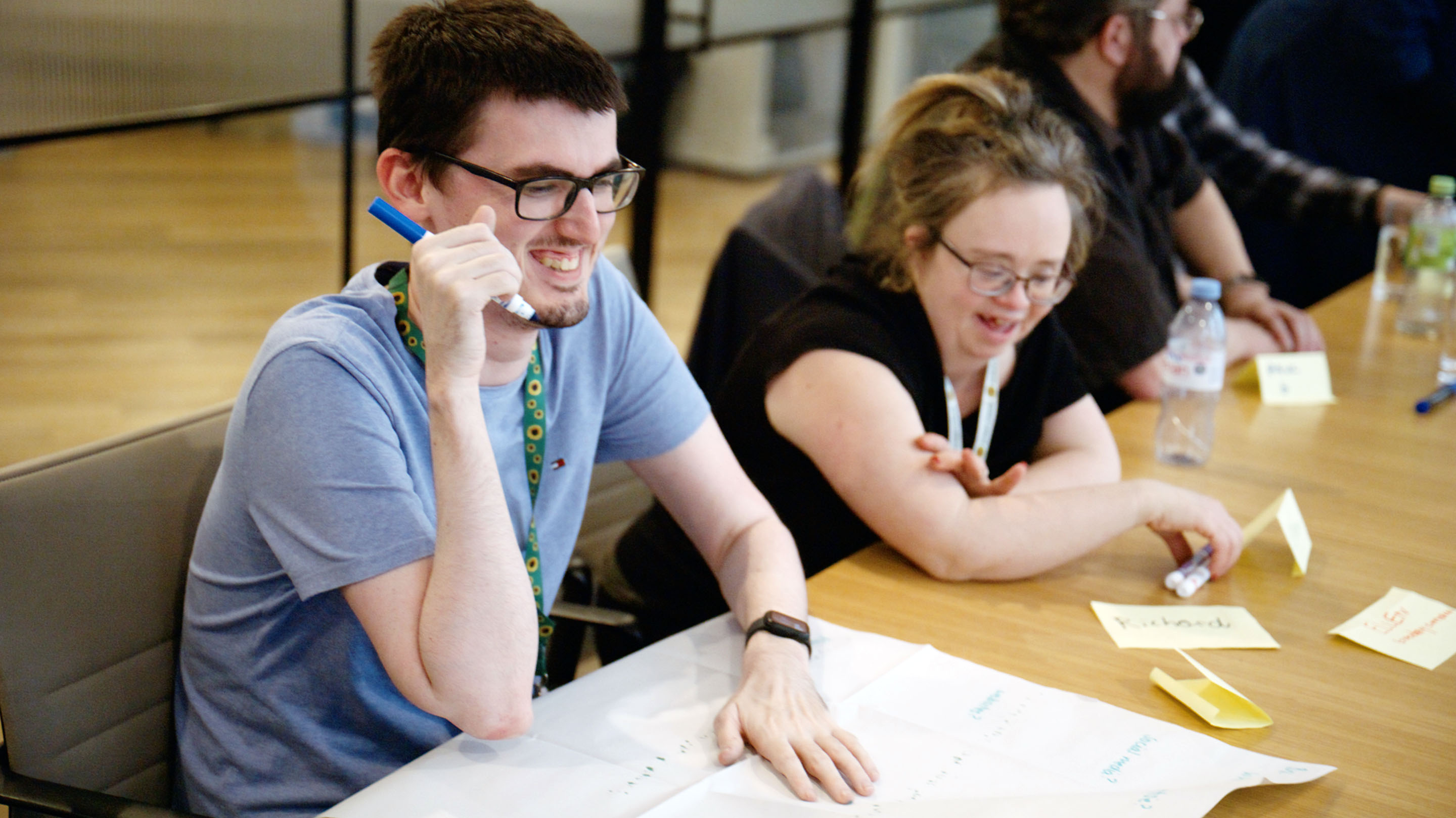 Mencap co-creation session. A man and a woman laughing while working together to write on a large piece of paper