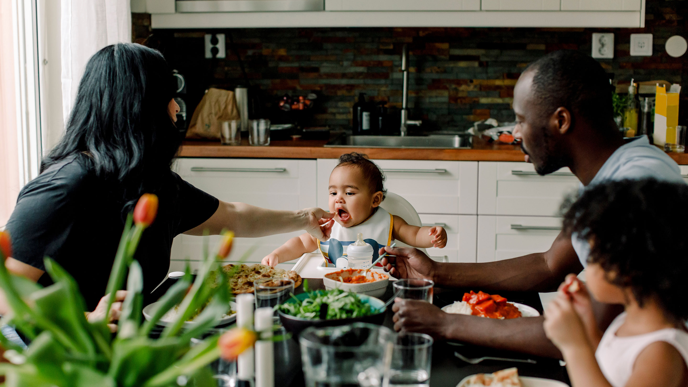 Mother feeding a baby in the kitchen with family