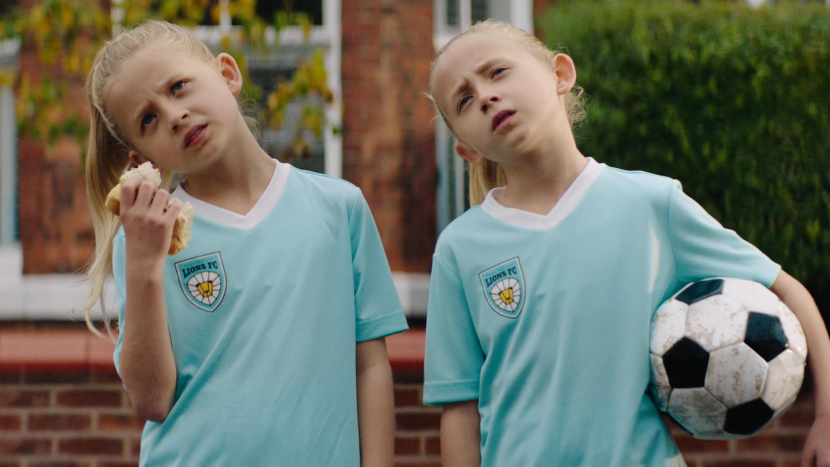 Pair of twins in football kit, both tilting their heads and looking confused