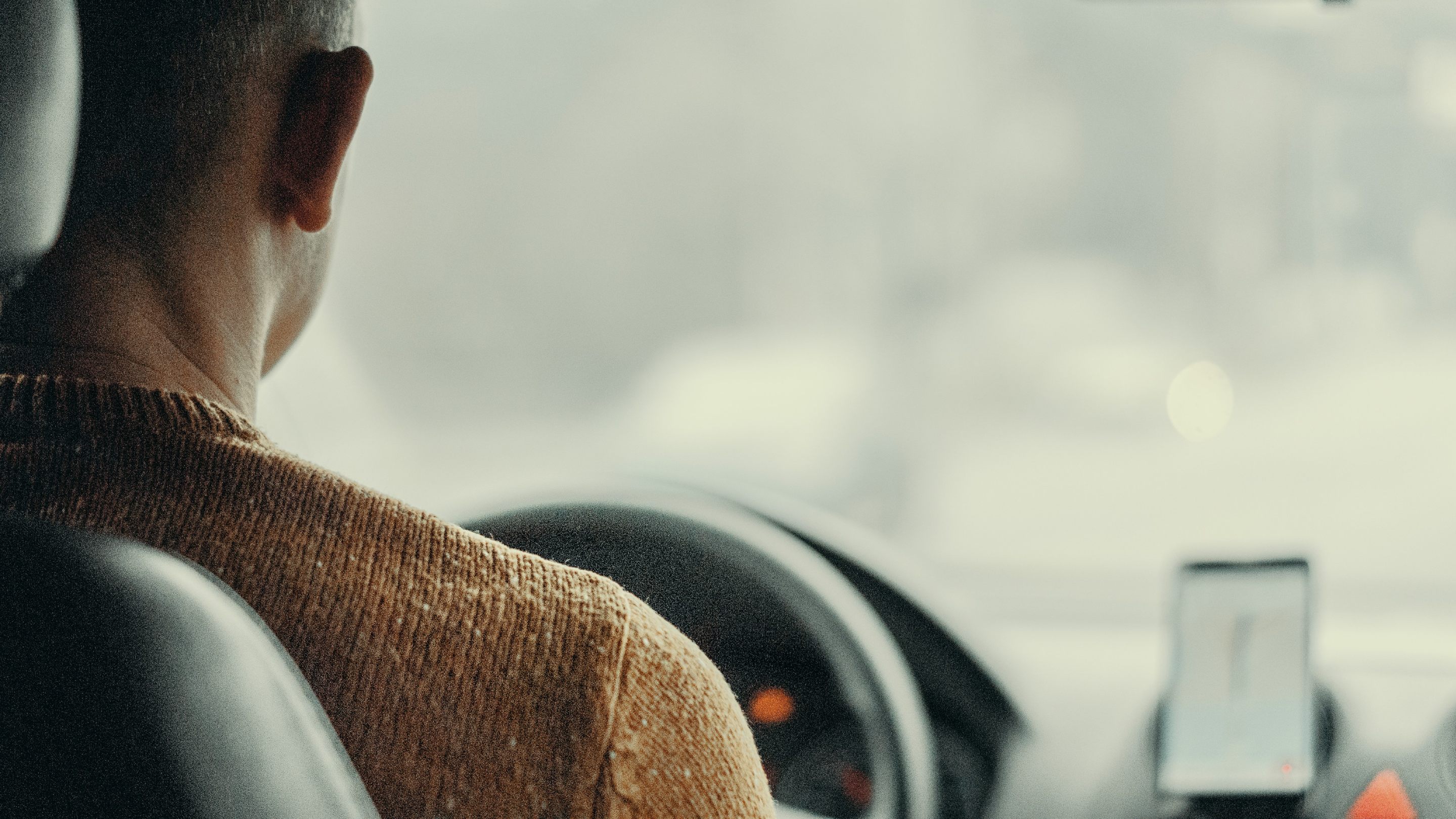 Person sitting in a car, viewed from behind, with a smartphone navigation app visible on the dashboard