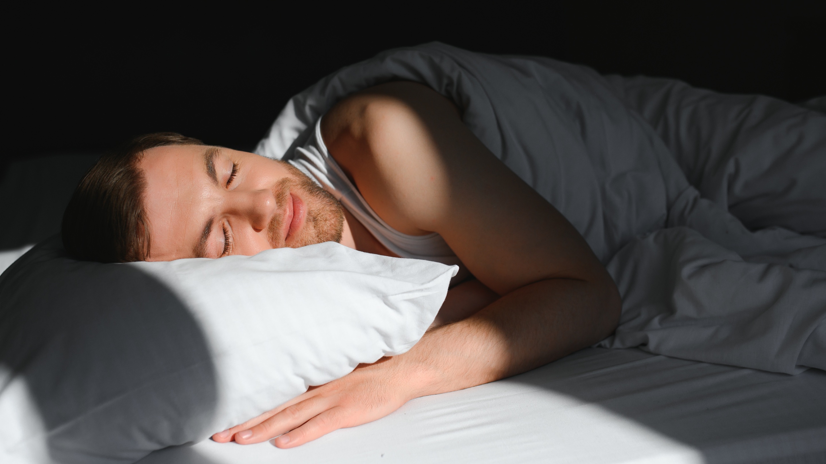 A person peacefully sleeping on a white pillow and bed, with sunlight casting soft shadows across the scene.