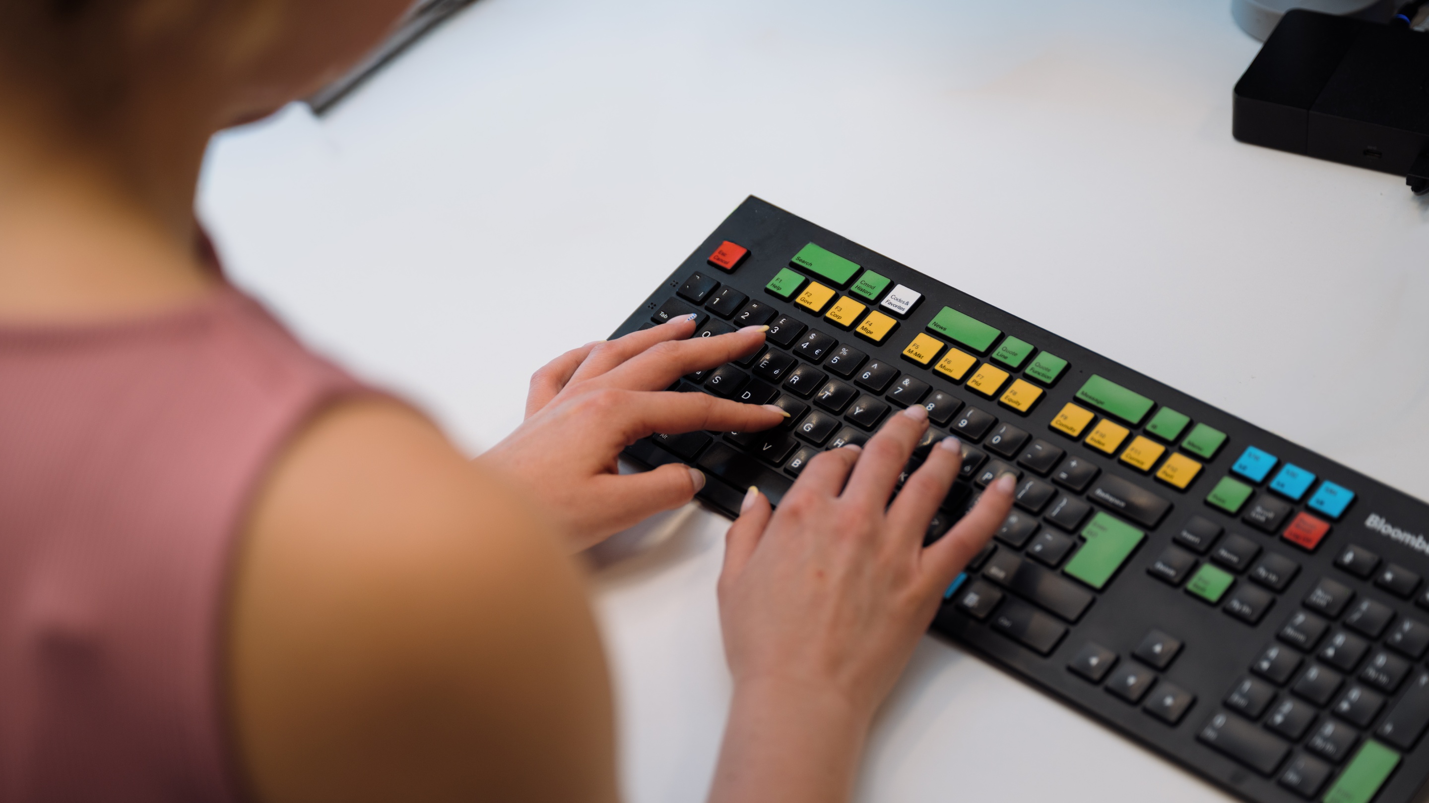 A person typing on a specialised keyboard with colourful keys, including green, yellow, blue, and red buttons, placed on a white desk.