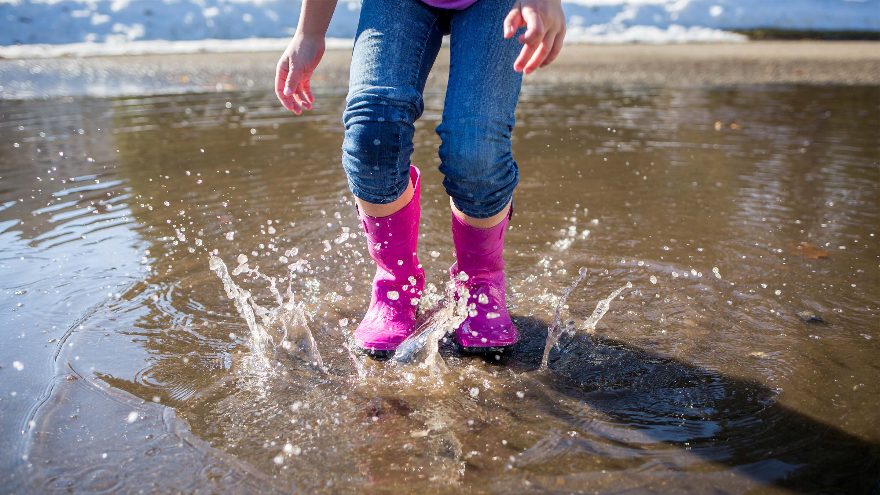 Child jumping in a puddle in pink wellies