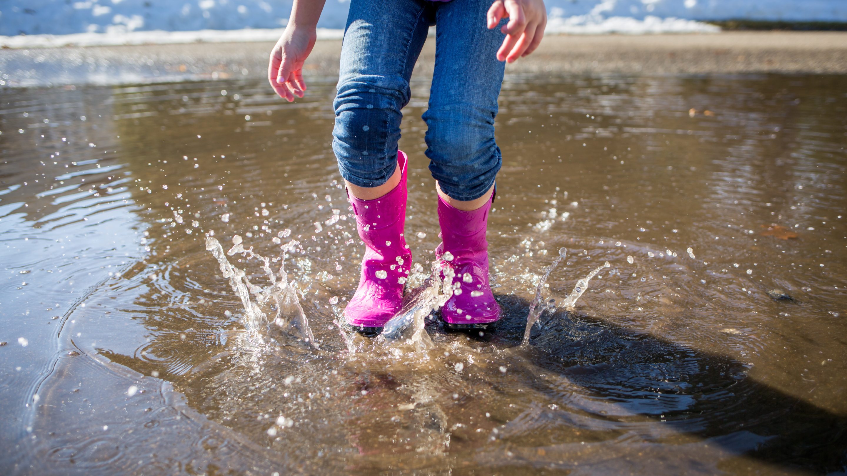 Person wearing pink wellington boots splashing in shallow water at the edge of a beach