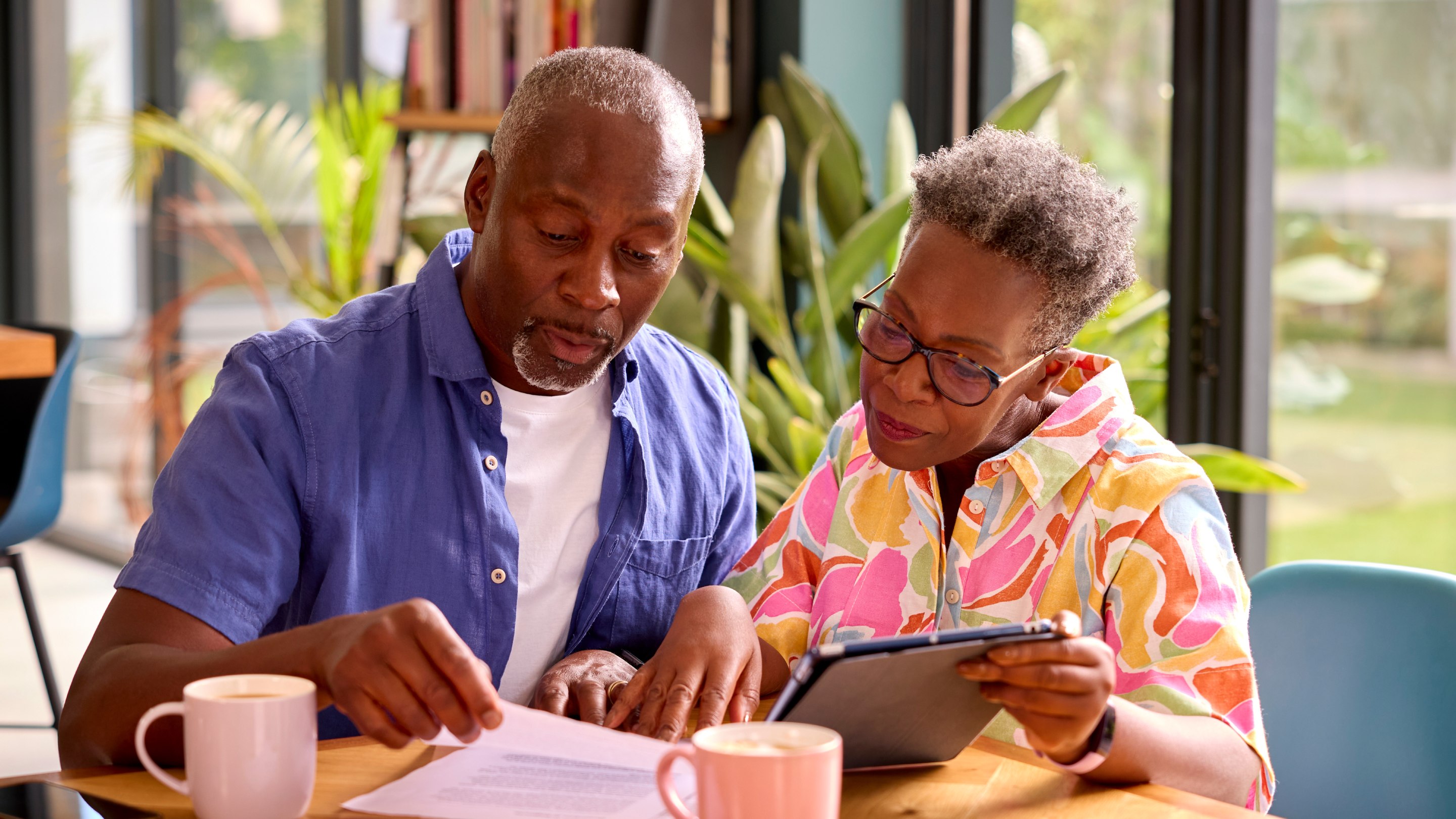 Senior couple sitting at a table and reviewing paperwork and finances on a tablet