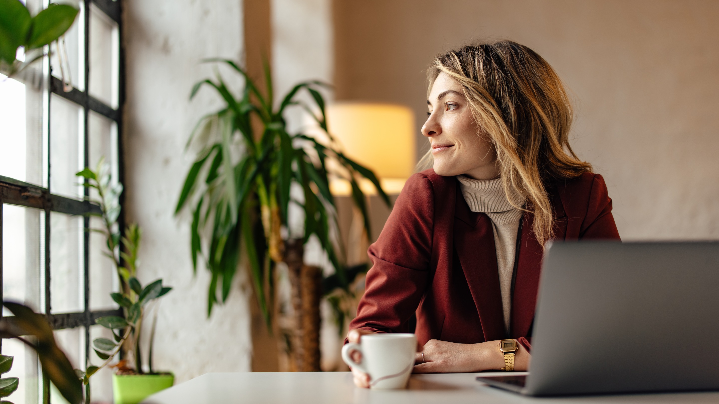 Smiling businesswoman sitting at laptop looking out window 