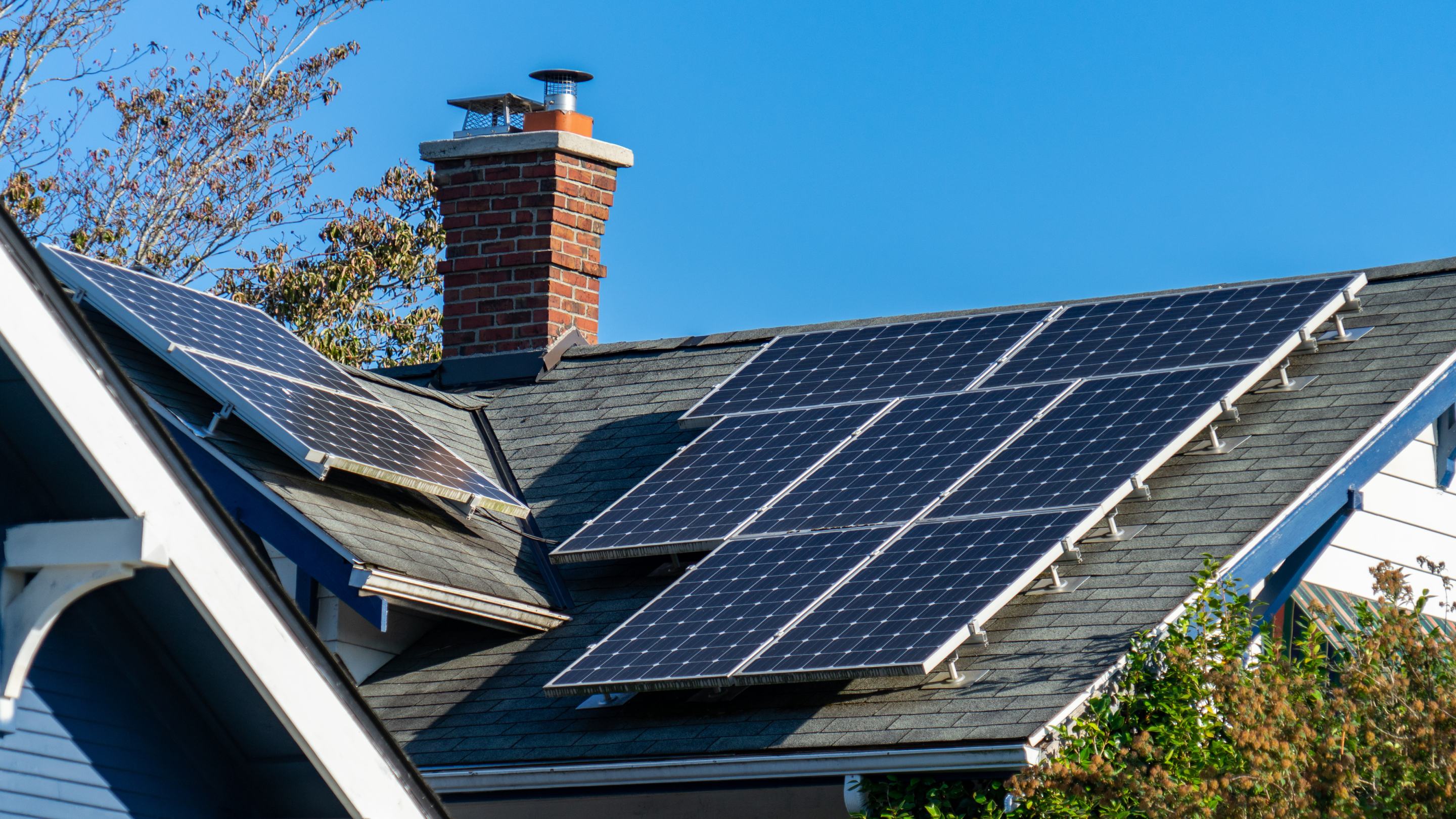 Multiple solar panels mounted on the roof of a residential property beneath a clear blue sky.