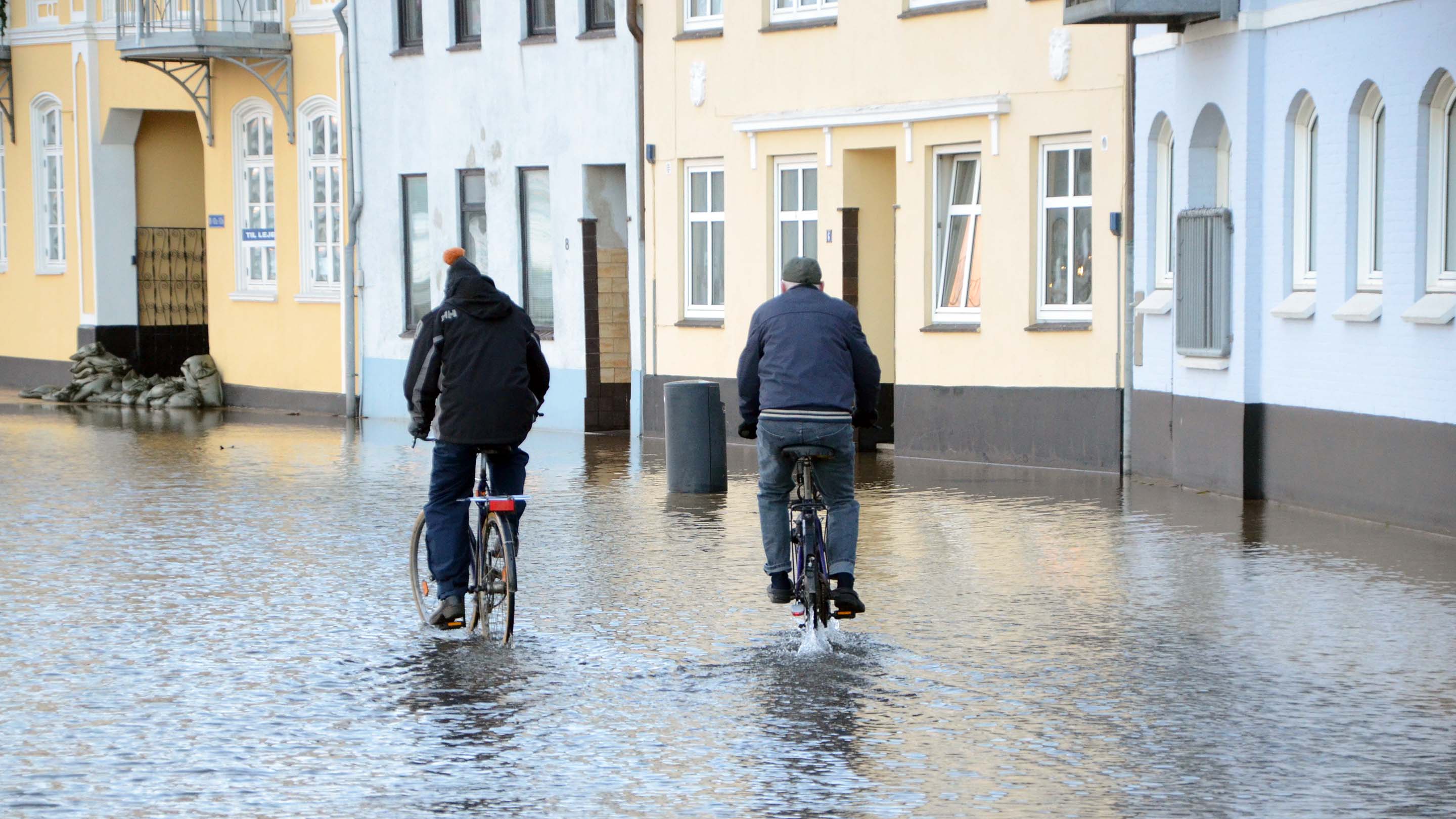 Two people ride bicycles through a flooded street