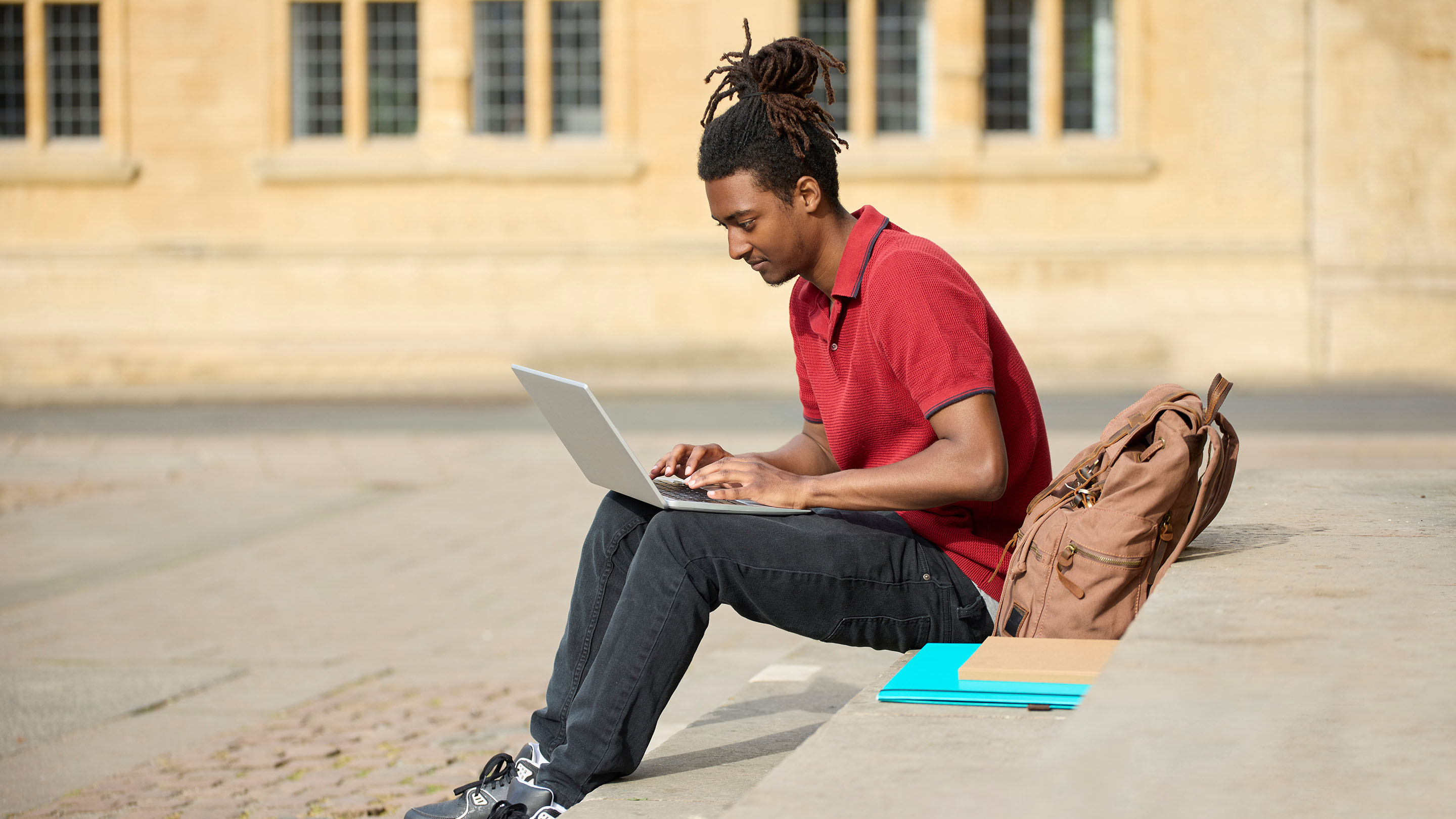 Student working on laptop sitting on steps outside university building