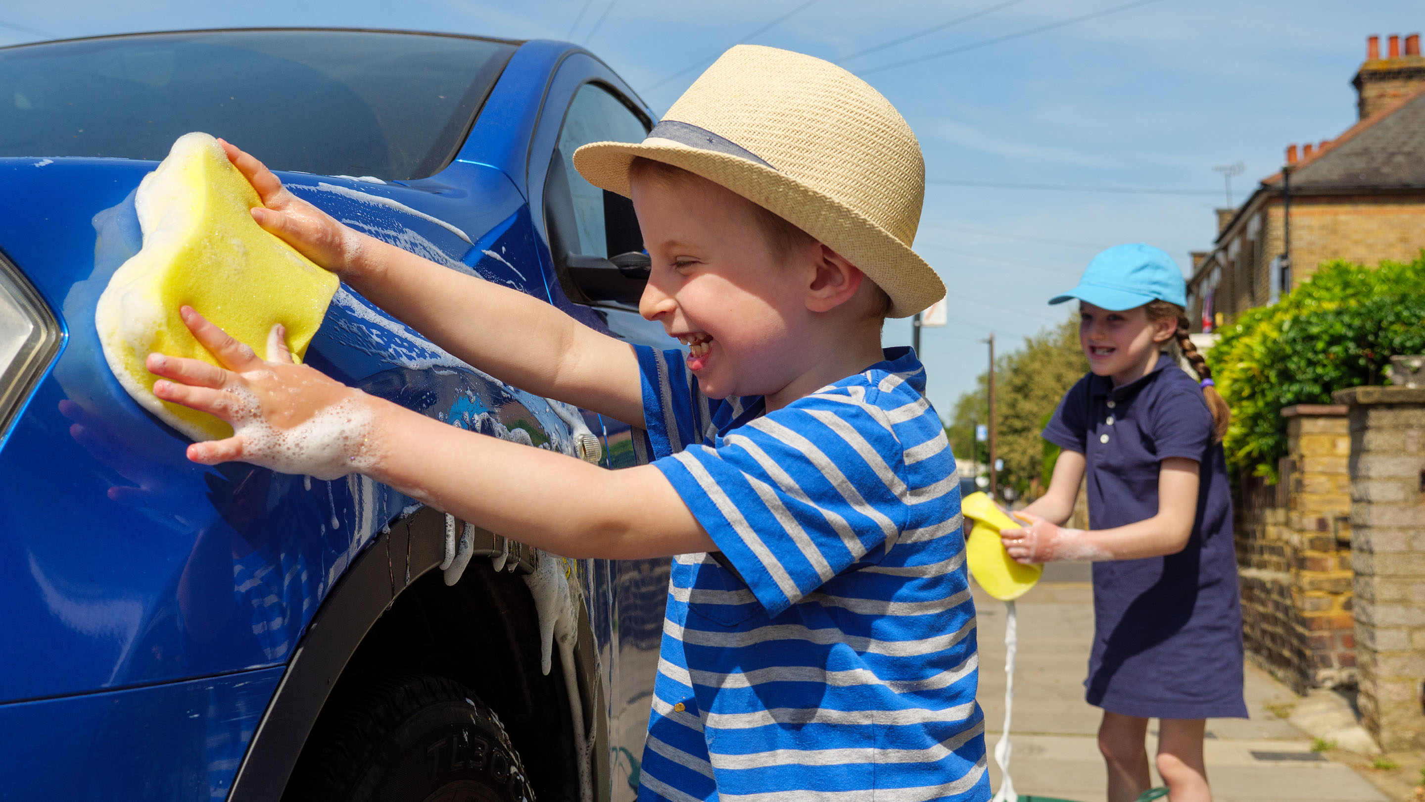 Two happy children having fun washing a car outside in the street