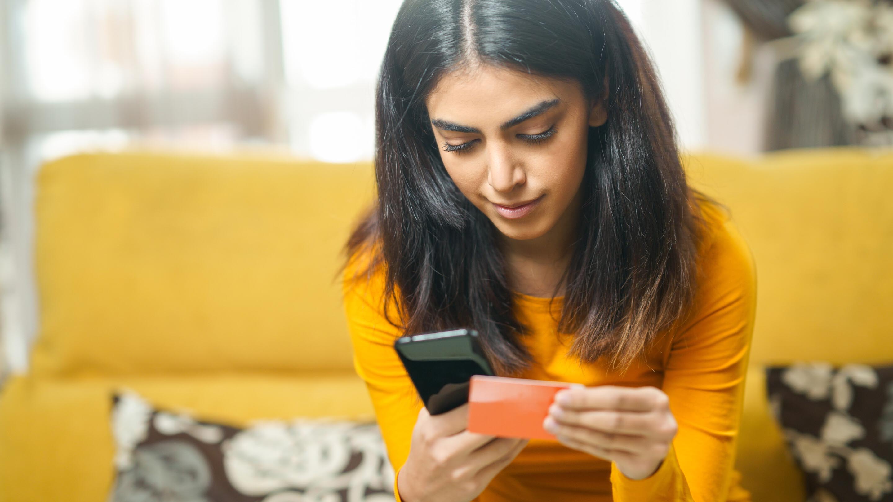 Woman using credit card and mobile phone sitting on sofa