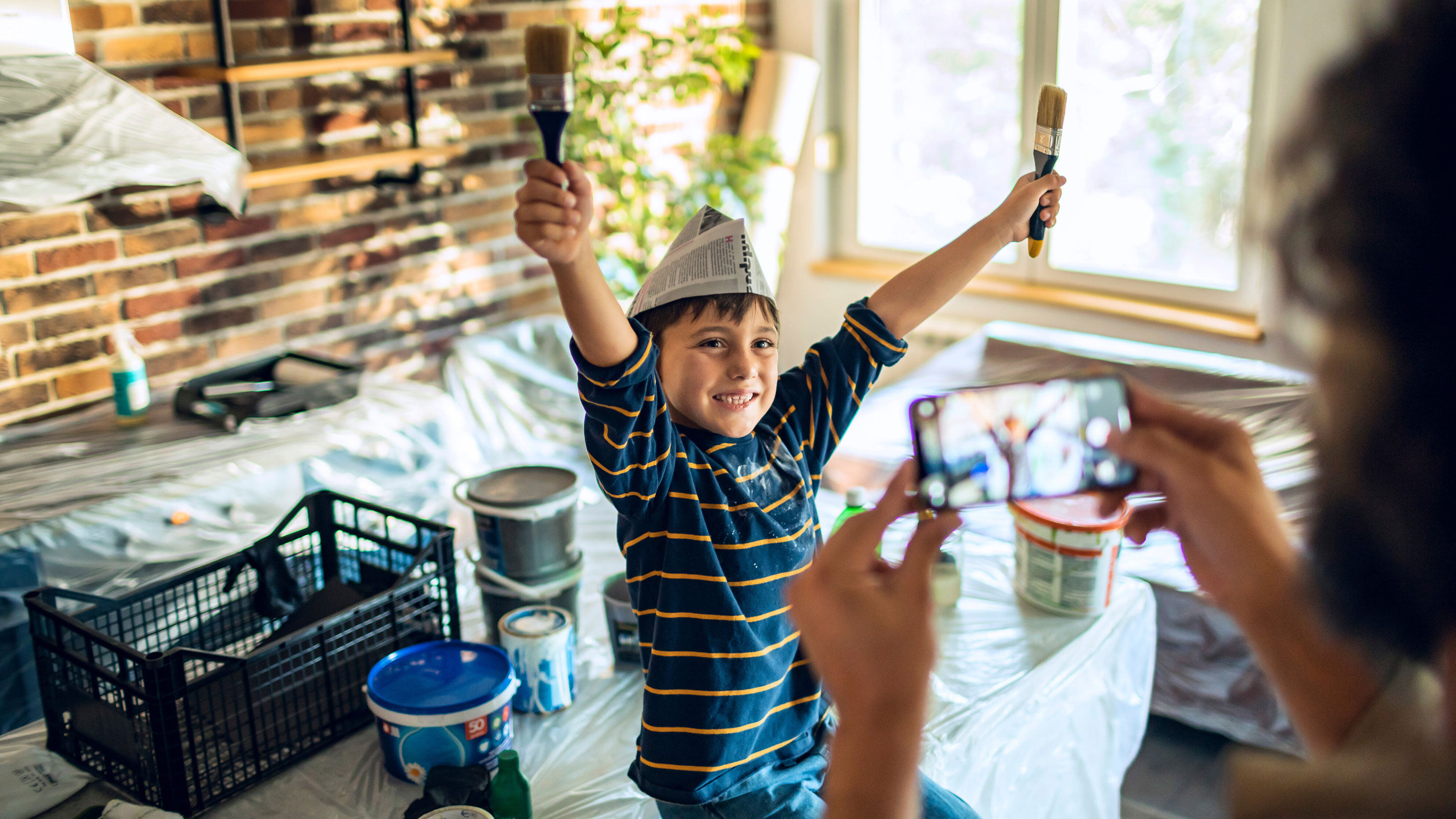 Young boy happily holding paintbrushes ready for home renovations