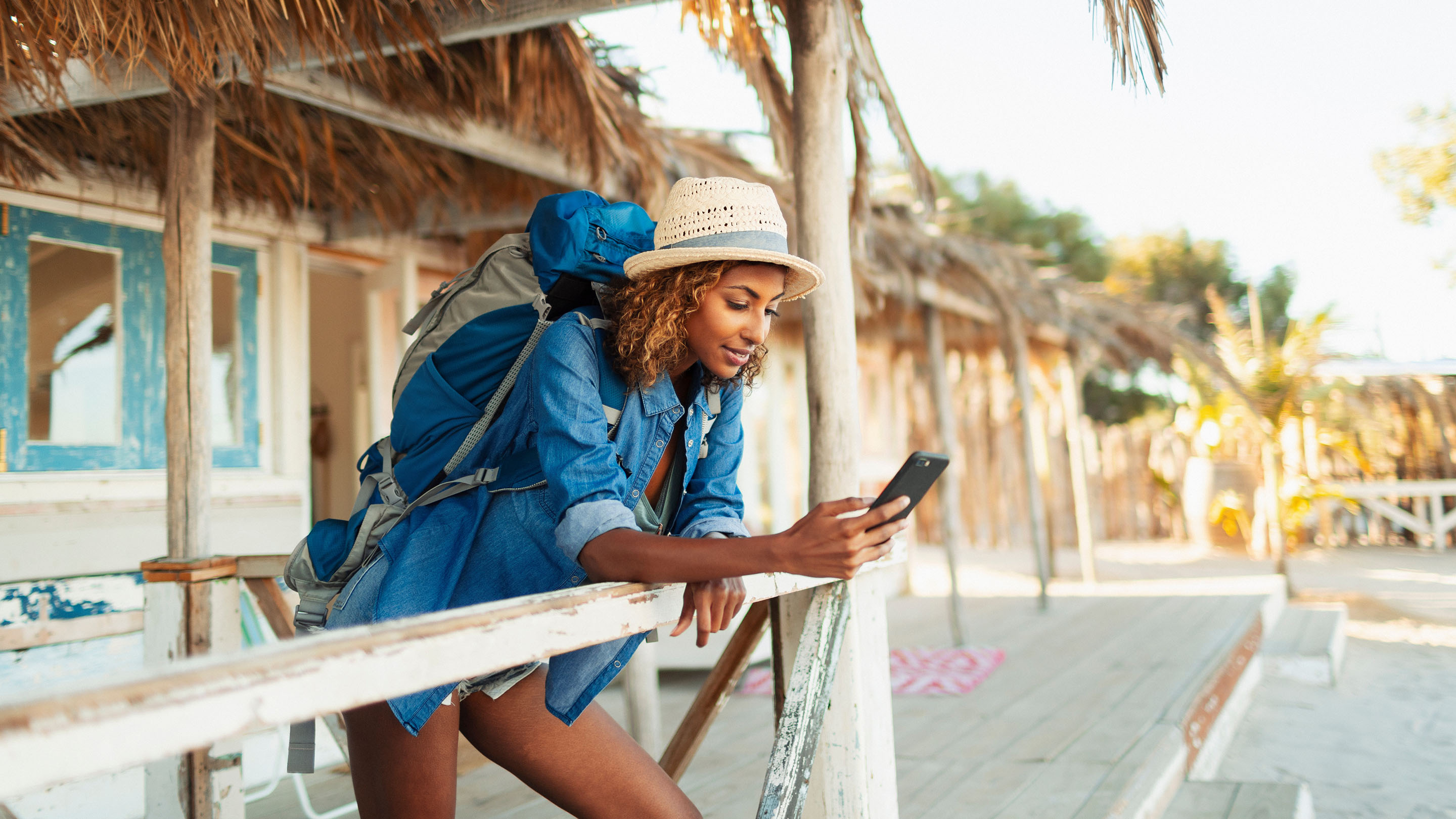 Young female backpacker using smart phone on beach hut patio