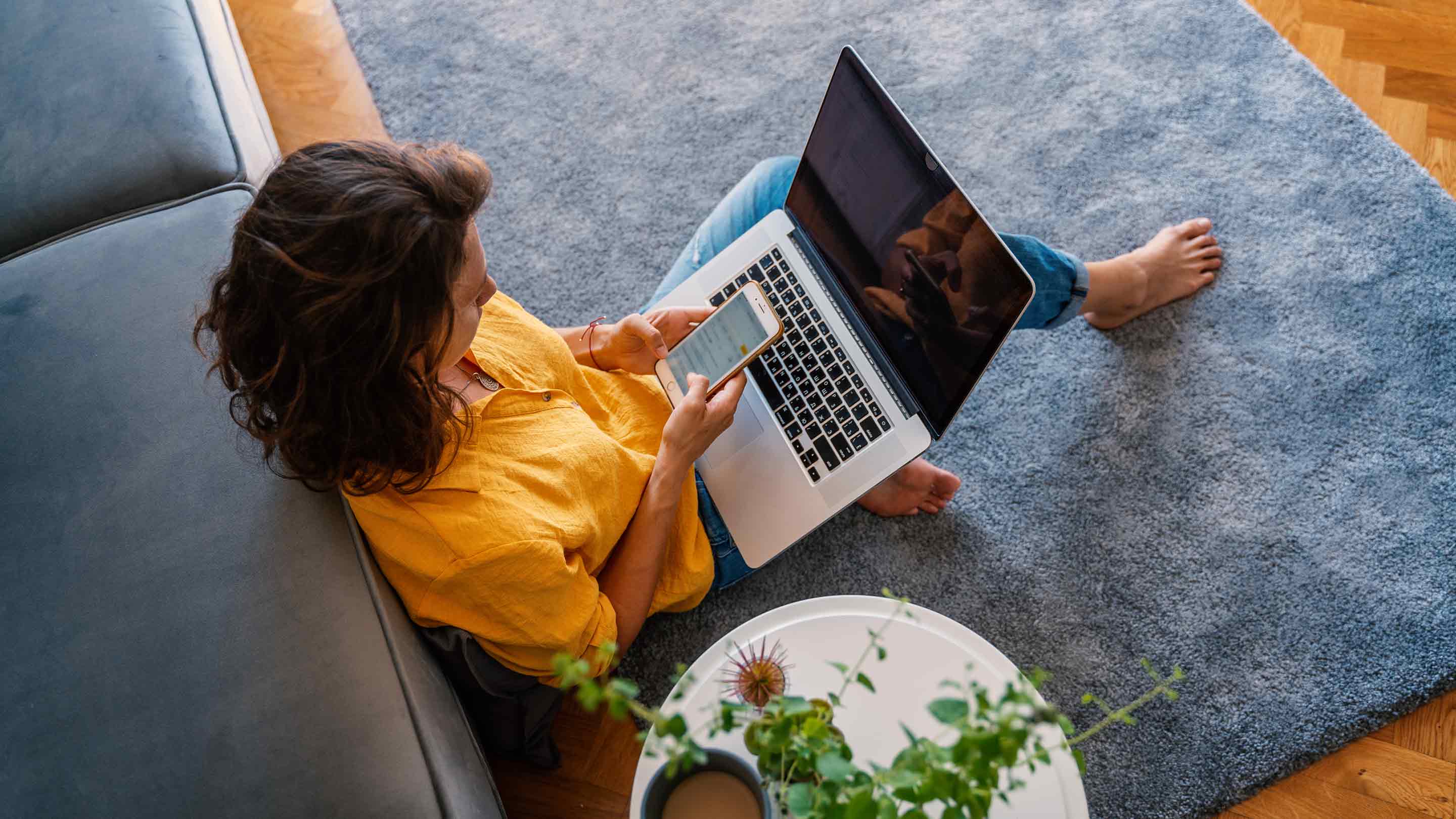 Young woman sitting on the floor with phone and laptop