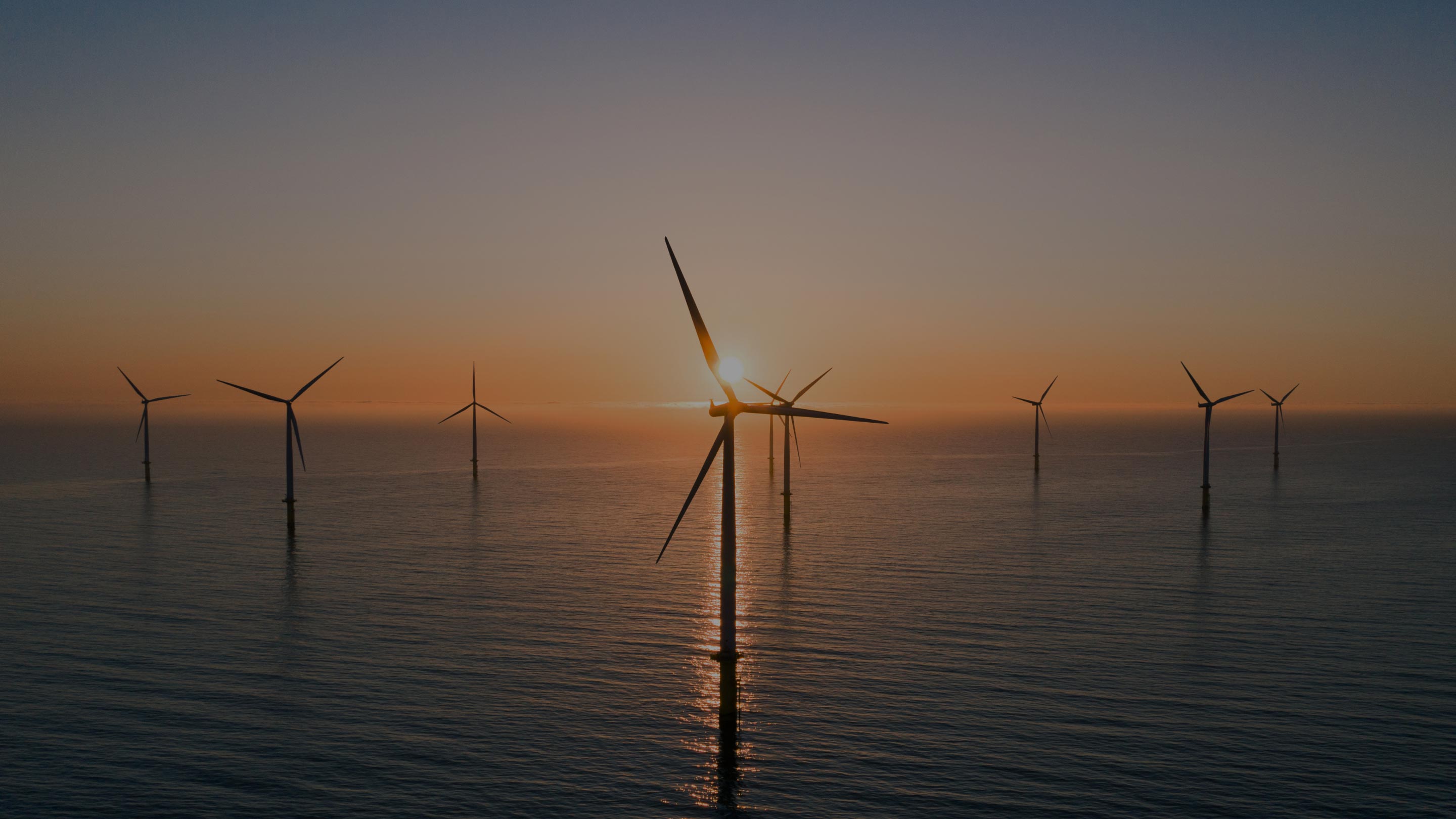 Wind turbines at sea with a sunrise behind them