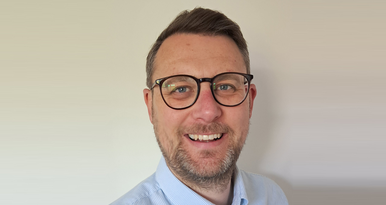 Black and White headshot of Dave Wheately, dark haired male wearing glasses.