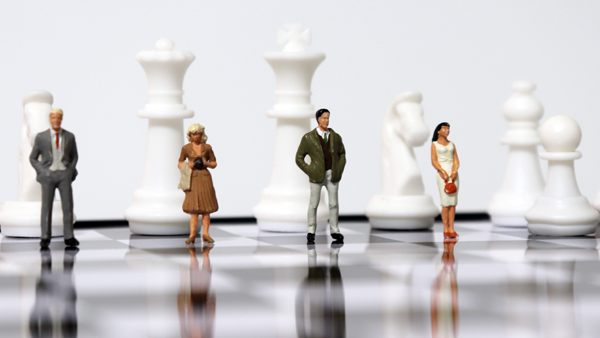 Miniature people standing with chess pieces on the chessboard