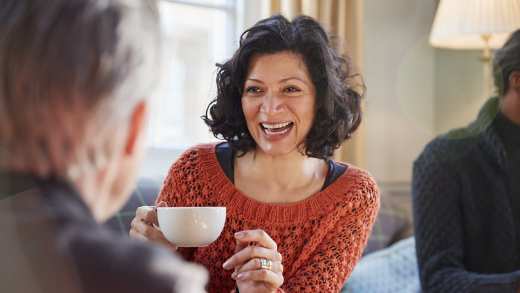 Middle aged woman wearing a red cardigan enjoying tea with friends