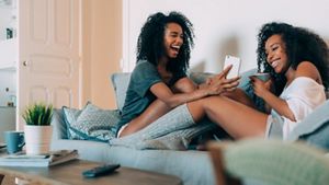 Two young black women on the sofa laughing at a phone
