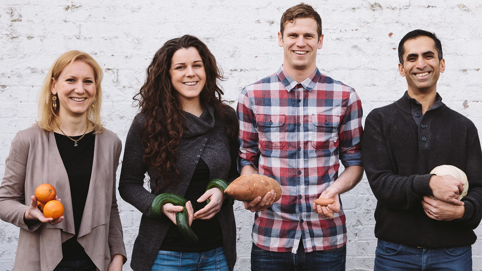 Image of four people standing and smiling at the camera holding different vegetables