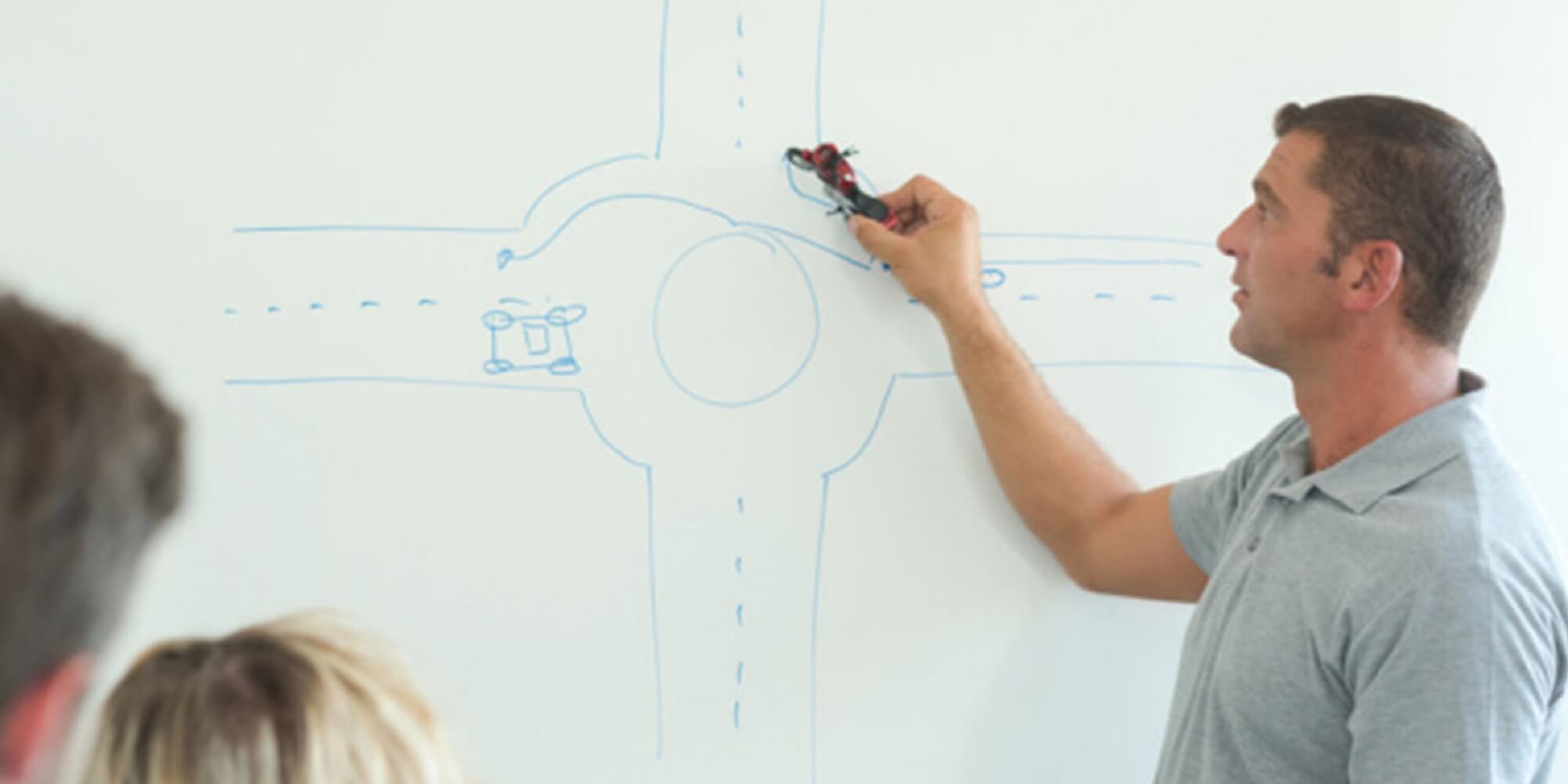 Teacher drawing on a white board how to approach a roundabout