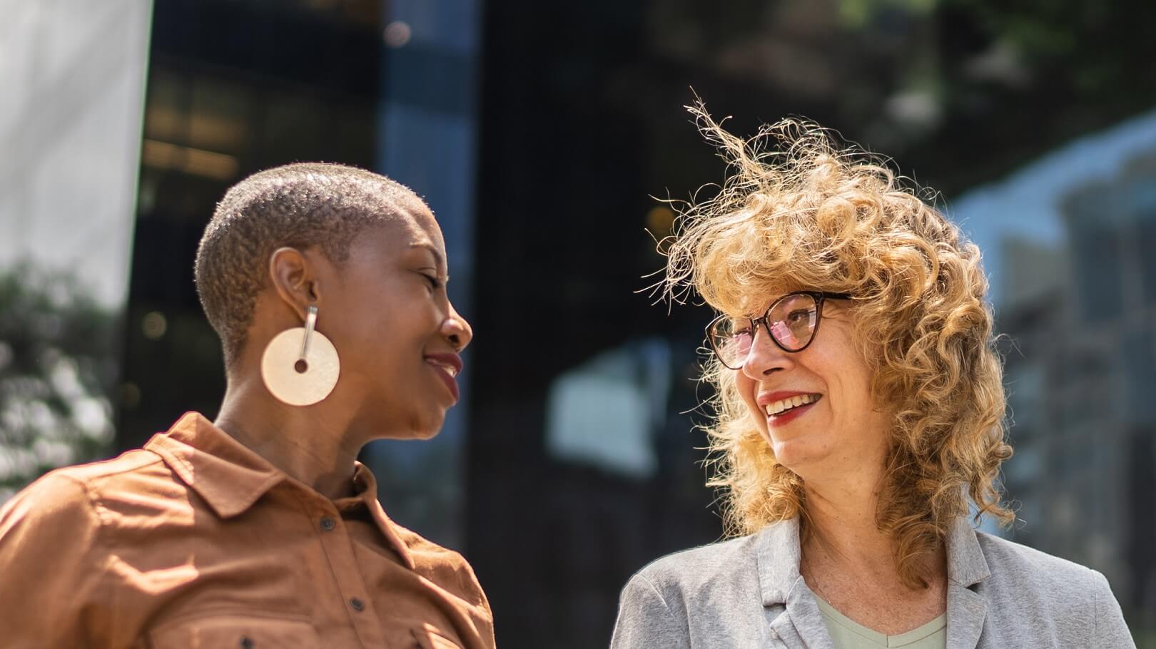 Two women looking at each other and smiling outside