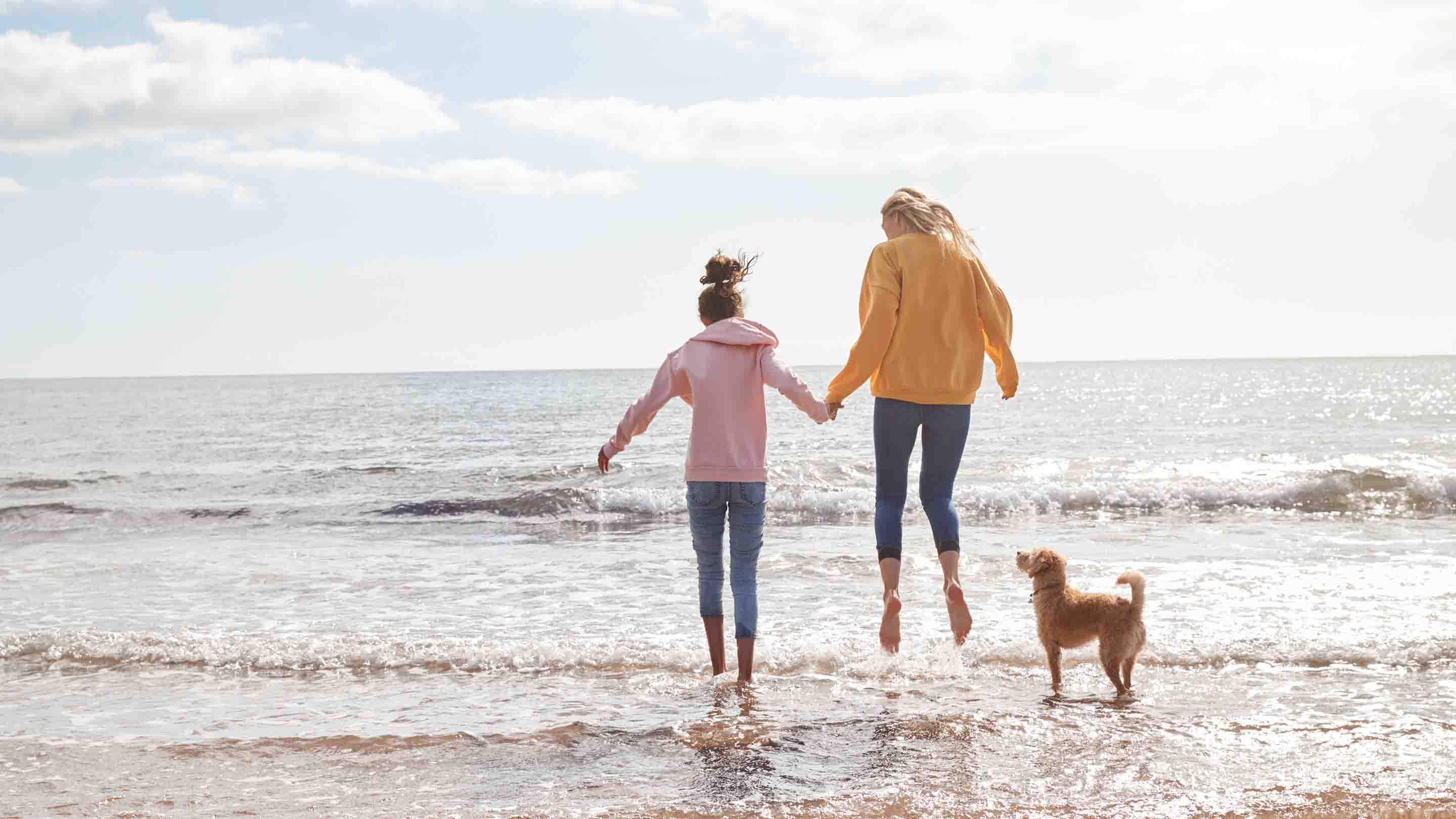 Mother and daughter jumping over the waves on a sunny day. 