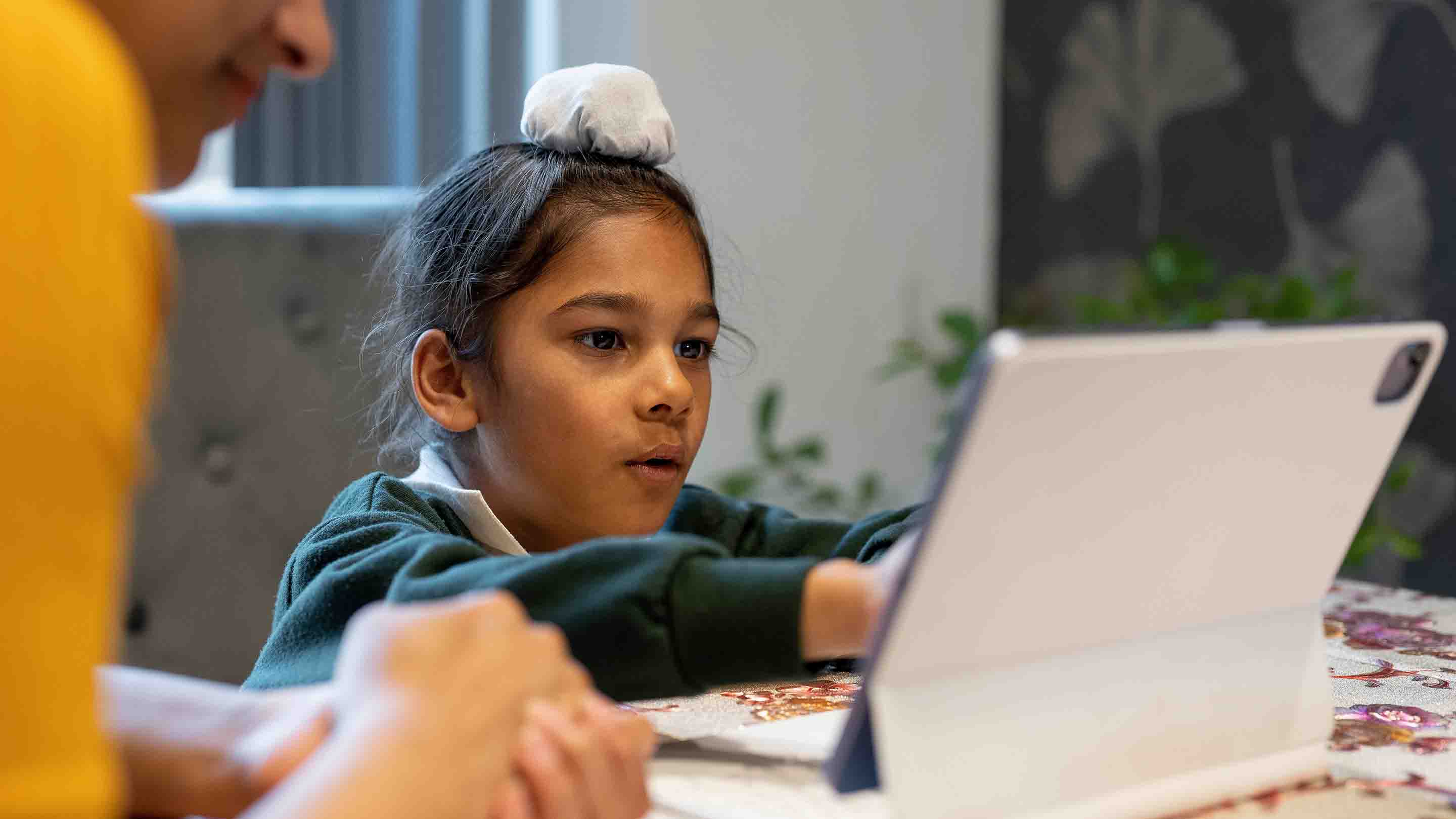 Child interacting with tablet with father looking over