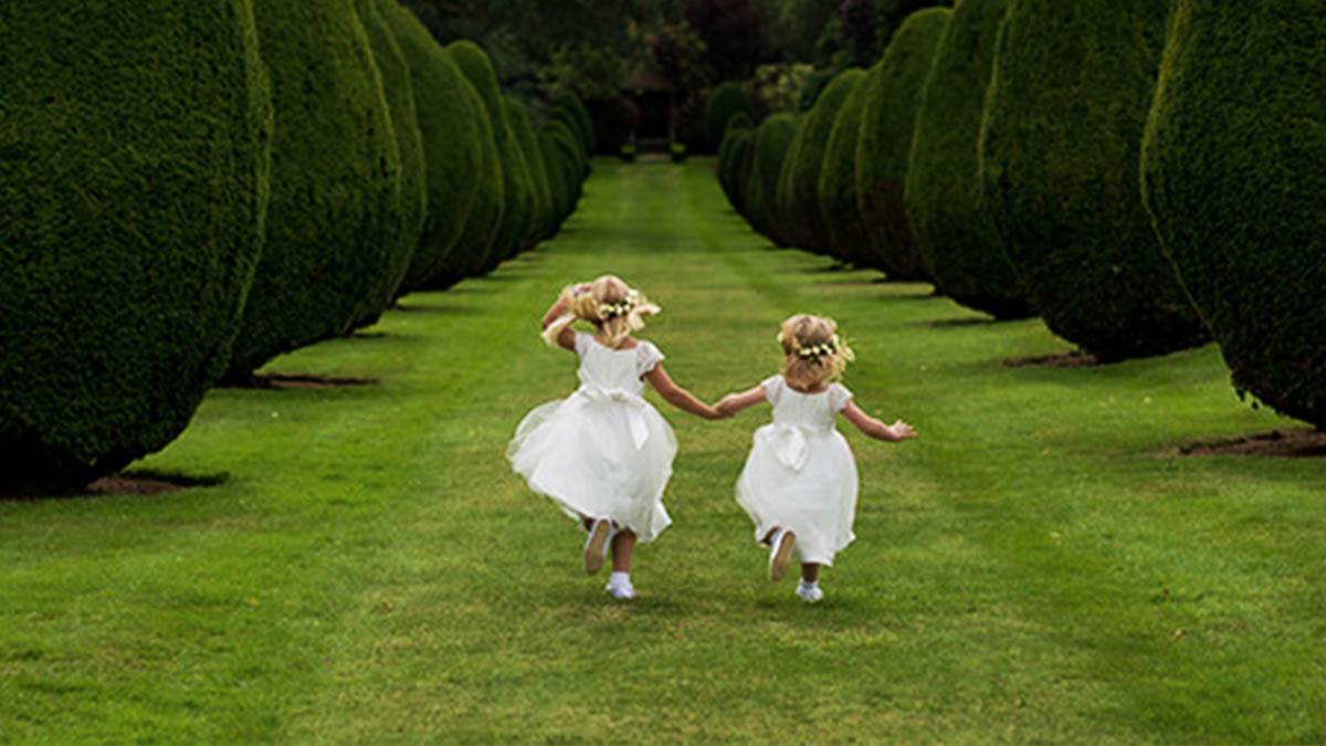 Ancient wedding traditions – 2 flower girls skipping on a bright day with tall green trees either side