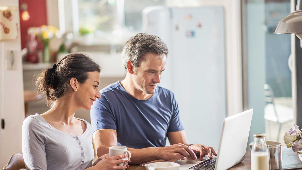 Couple happy at home checking how much life insurance they need on their laptop